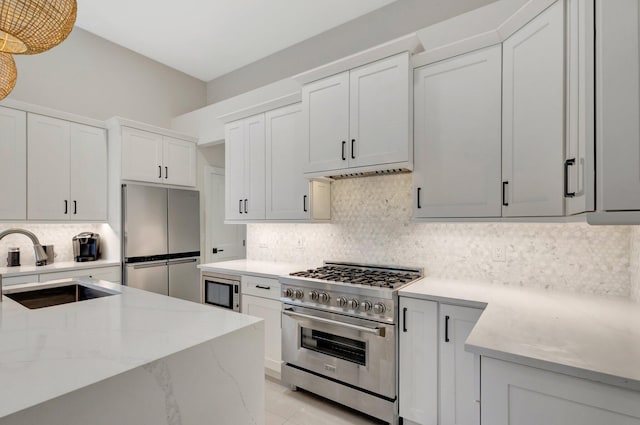 kitchen featuring white cabinets, light stone counters, appliances with stainless steel finishes, a sink, and backsplash