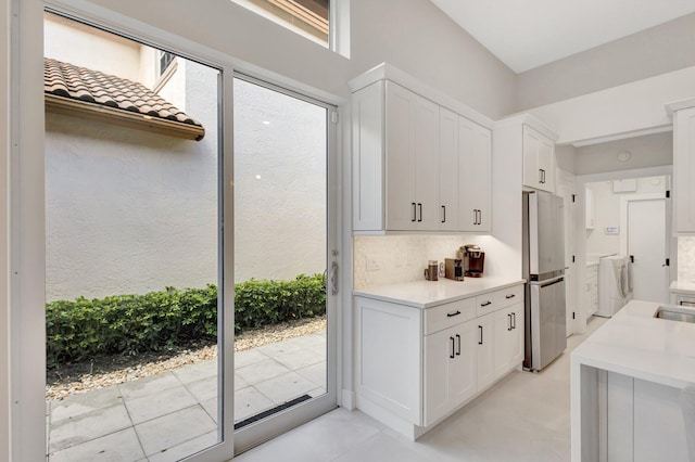 interior space with washing machine and dryer, white cabinets, light countertops, freestanding refrigerator, and decorative backsplash