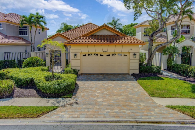 mediterranean / spanish house with a garage, a tile roof, fence, and decorative driveway