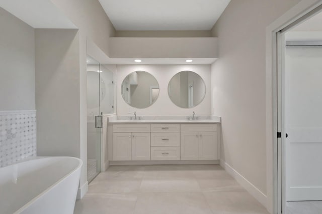 bathroom featuring double vanity, a sink, a shower stall, a freestanding tub, and baseboards