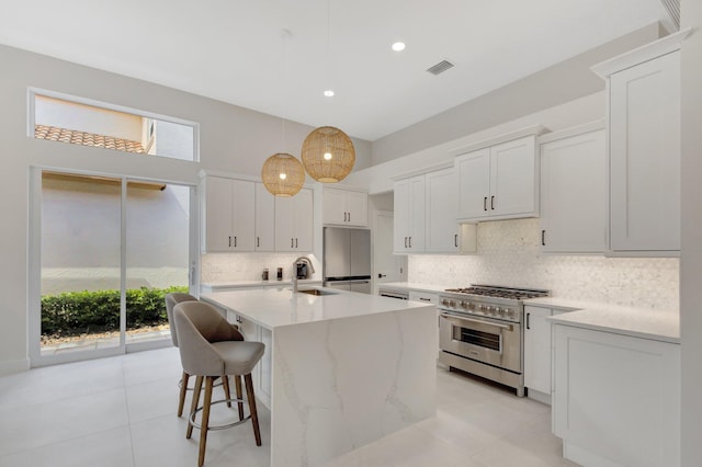 kitchen featuring visible vents, refrigerator, high end stainless steel range, a kitchen island with sink, and backsplash