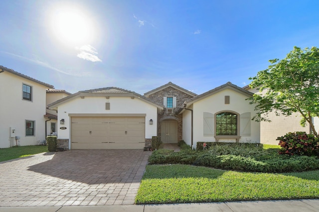 mediterranean / spanish home featuring decorative driveway, stone siding, a garage, and stucco siding