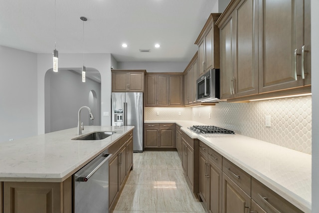 kitchen with arched walkways, light stone counters, appliances with stainless steel finishes, a sink, and backsplash