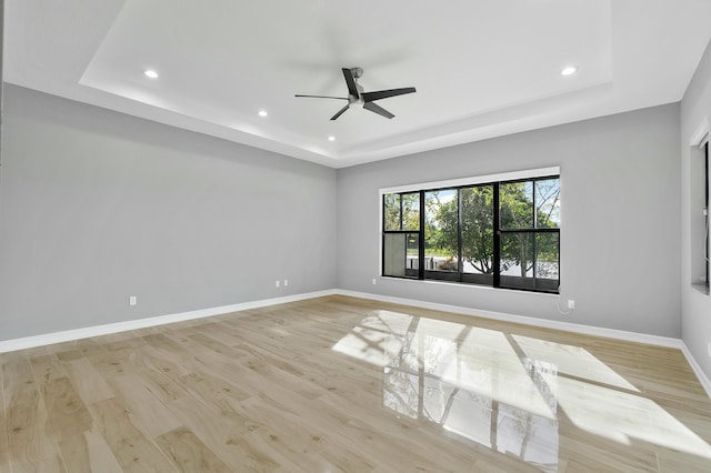 spare room with a tray ceiling, recessed lighting, a ceiling fan, light wood-type flooring, and baseboards