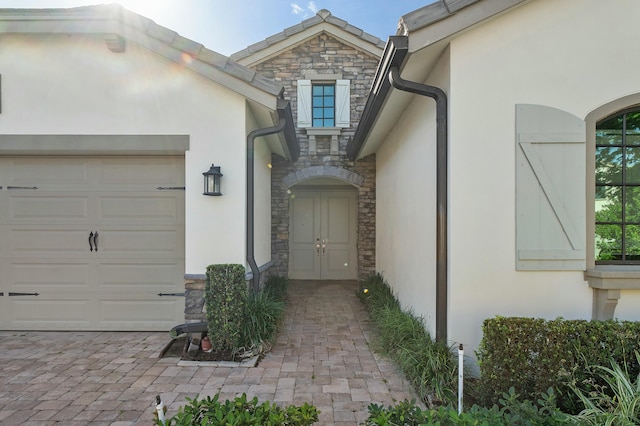 doorway to property featuring a garage, stone siding, and stucco siding