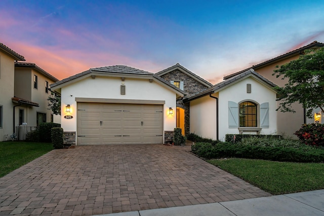 view of front of house with a garage, stone siding, decorative driveway, and stucco siding