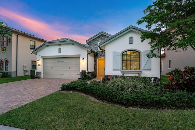 view of front facade featuring decorative driveway, stucco siding, an attached garage, a front yard, and stone siding