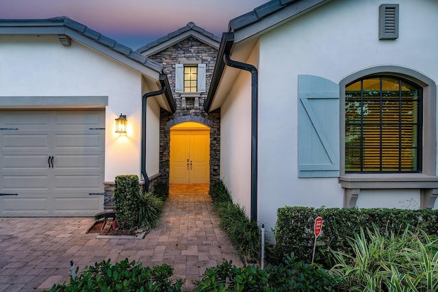 view of exterior entry with an attached garage, stone siding, and stucco siding