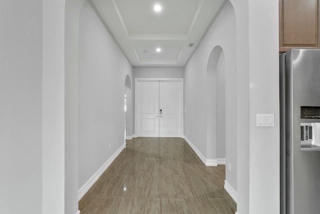 corridor featuring baseboards, arched walkways, a tray ceiling, and recessed lighting