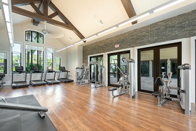 gym featuring french doors, visible vents, light wood-style floors, brick wall, and high vaulted ceiling