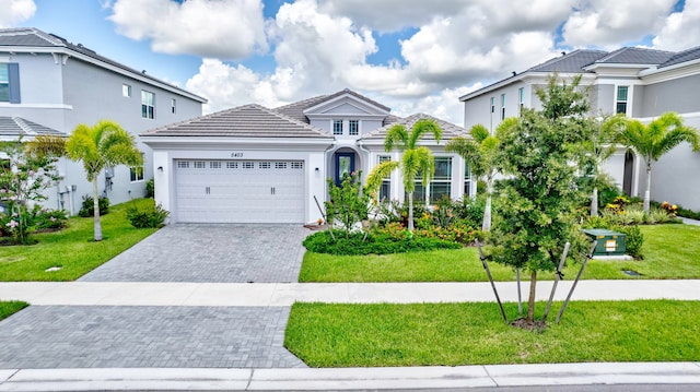 view of front of home featuring an attached garage, a tile roof, a front lawn, and decorative driveway