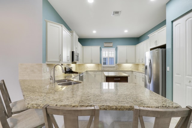 kitchen with appliances with stainless steel finishes, white cabinetry, a sink, a peninsula, and a kitchen bar