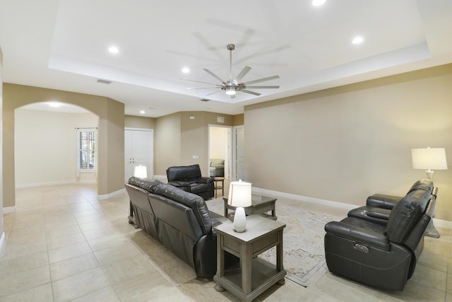 living area featuring arched walkways, a tray ceiling, visible vents, and baseboards