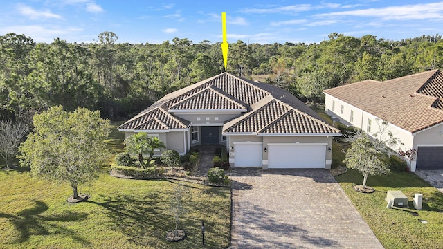 mediterranean / spanish-style home featuring a tile roof, an attached garage, decorative driveway, a front lawn, and stucco siding