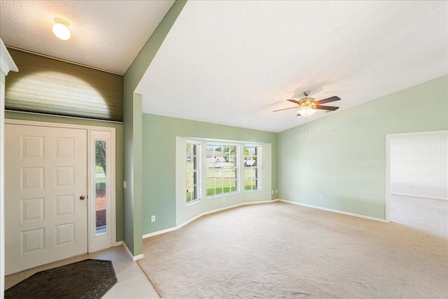 foyer entrance featuring a ceiling fan, light carpet, vaulted ceiling, a textured ceiling, and baseboards