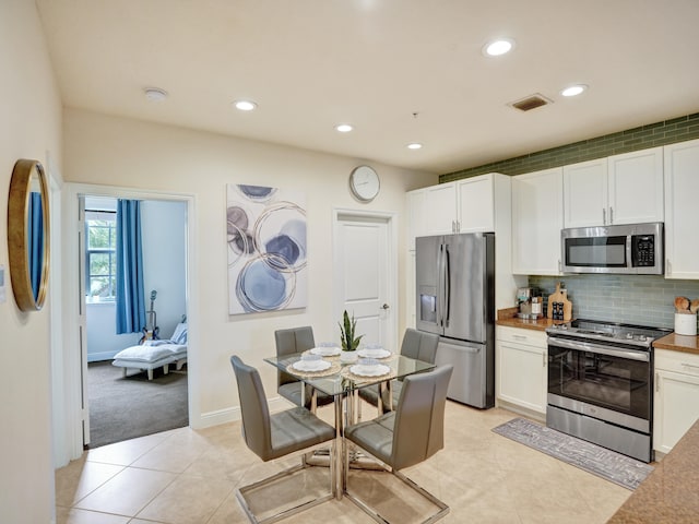 kitchen with light tile patterned flooring, stainless steel appliances, visible vents, white cabinetry, and tasteful backsplash