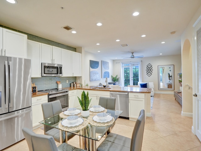 kitchen featuring backsplash, appliances with stainless steel finishes, light tile patterned flooring, a sink, and a peninsula