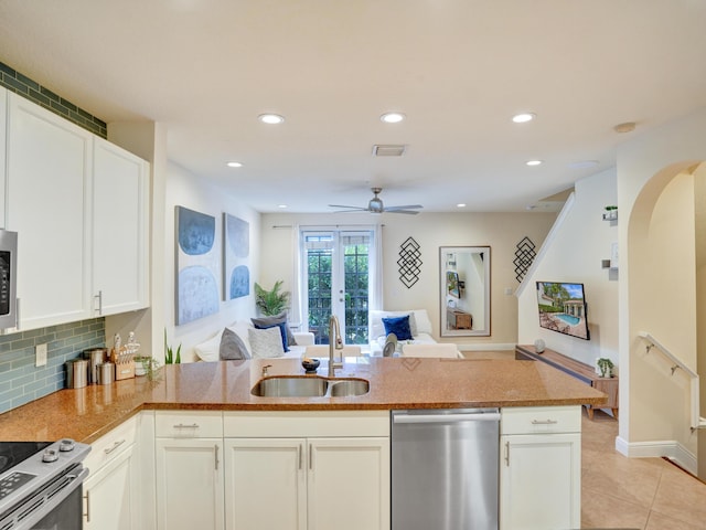 kitchen with light tile patterned flooring, a sink, open floor plan, appliances with stainless steel finishes, and decorative backsplash