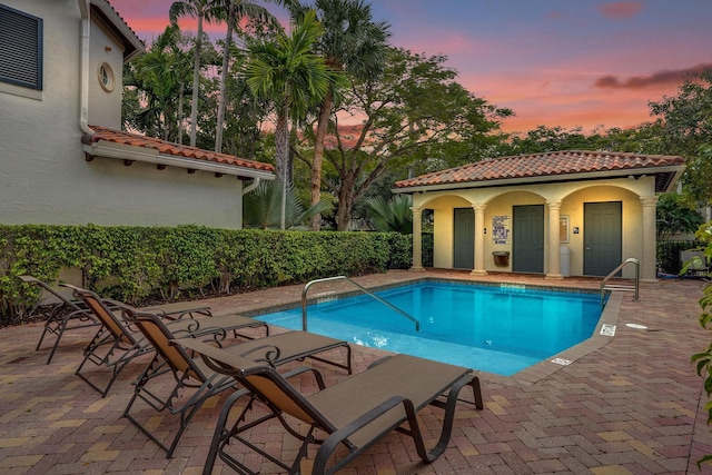 pool at dusk with an outdoor structure, a patio, and a community pool