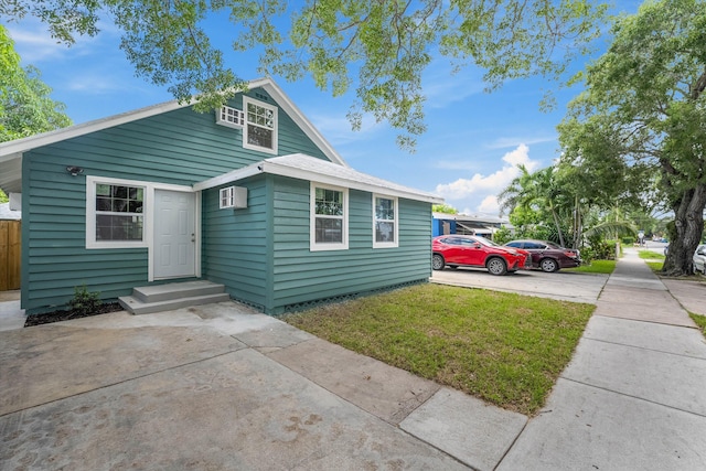 bungalow featuring a front yard, fence, concrete driveway, and a wall mounted air conditioner