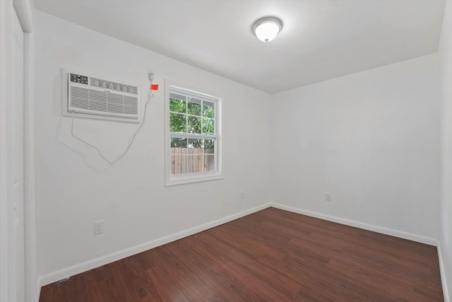 spare room with dark wood-style floors, a wall unit AC, and baseboards