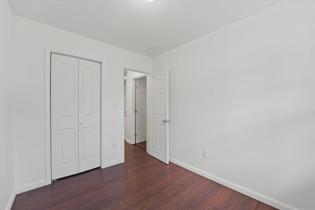 unfurnished bedroom featuring dark wood-style floors, a closet, and baseboards