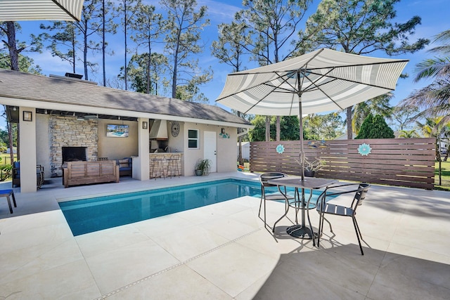 view of pool with a patio, an outdoor structure, fence, outdoor dry bar, and an outdoor living space with a fireplace