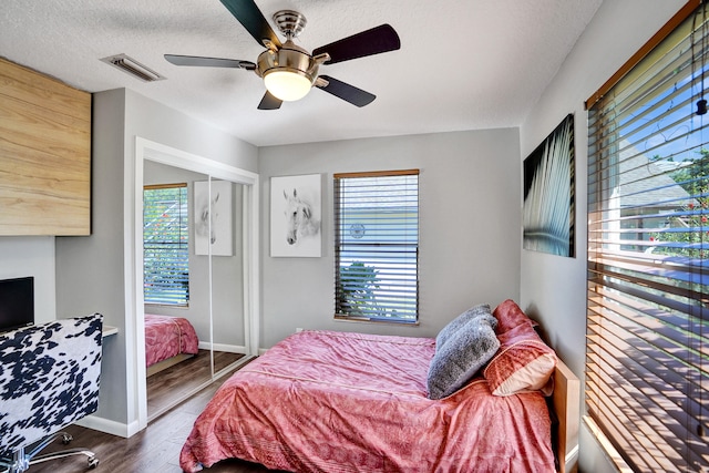 bedroom with a textured ceiling, wood finished floors, visible vents, baseboards, and a closet