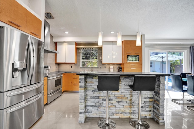 kitchen with tasteful backsplash, visible vents, wall chimney exhaust hood, appliances with stainless steel finishes, and a kitchen bar