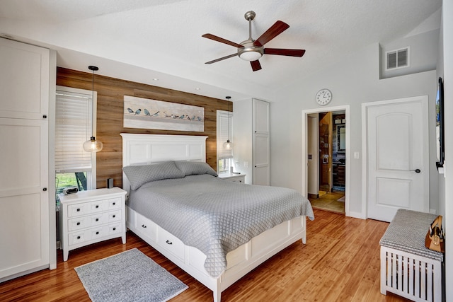 bedroom with visible vents, a ceiling fan, lofted ceiling, wood walls, and light wood-style floors