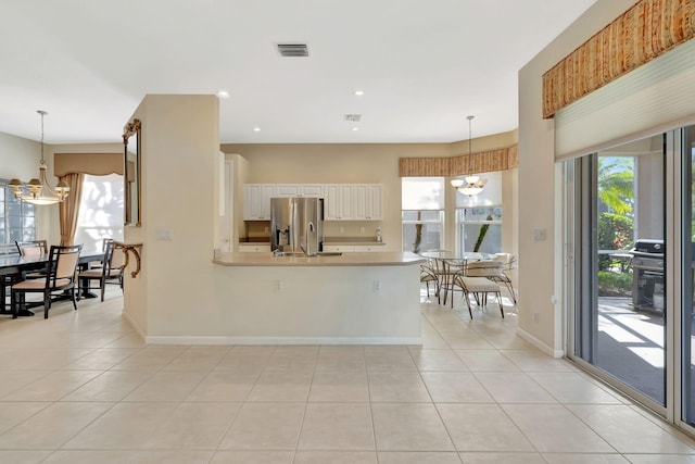 kitchen with stainless steel fridge, a peninsula, an inviting chandelier, a healthy amount of sunlight, and light tile patterned flooring