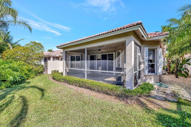 back of house featuring a sunroom, ceiling fan, a tiled roof, a yard, and stucco siding