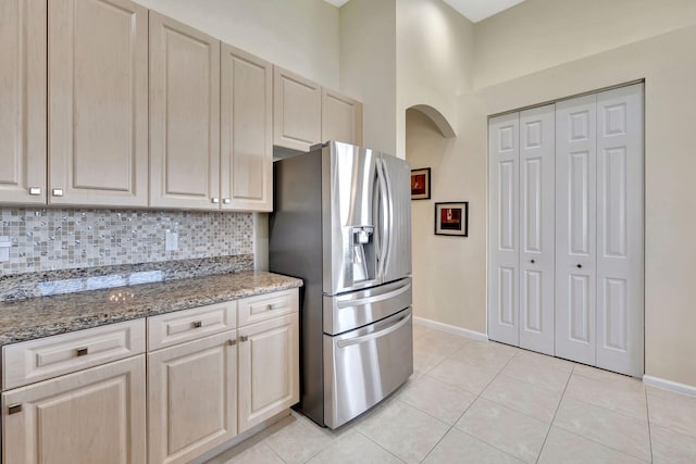 kitchen featuring arched walkways, light tile patterned floors, stainless steel refrigerator with ice dispenser, and decorative backsplash