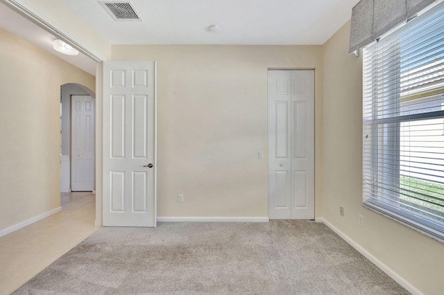 unfurnished bedroom featuring multiple windows, visible vents, arched walkways, and carpet flooring