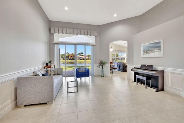 living area featuring light tile patterned flooring, arched walkways, a decorative wall, and wainscoting