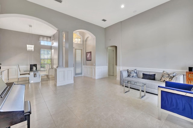 living room featuring light tile patterned floors, decorative columns, a towering ceiling, a wainscoted wall, and a decorative wall