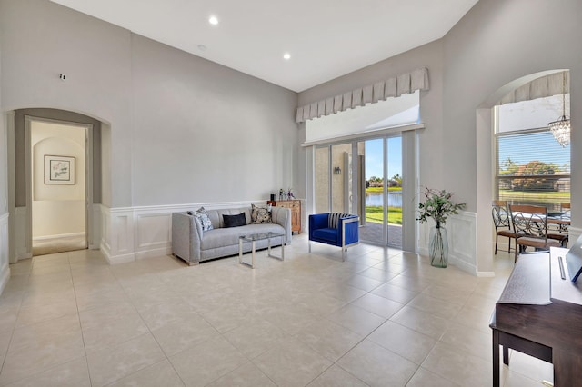 living area featuring arched walkways, a wainscoted wall, a decorative wall, and light tile patterned floors