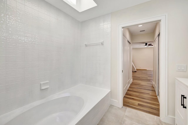 bathroom featuring tile patterned flooring, baseboards, a skylight, and a tub to relax in