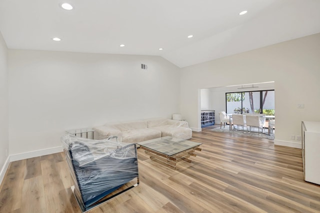 living area featuring lofted ceiling, visible vents, baseboards, and light wood finished floors