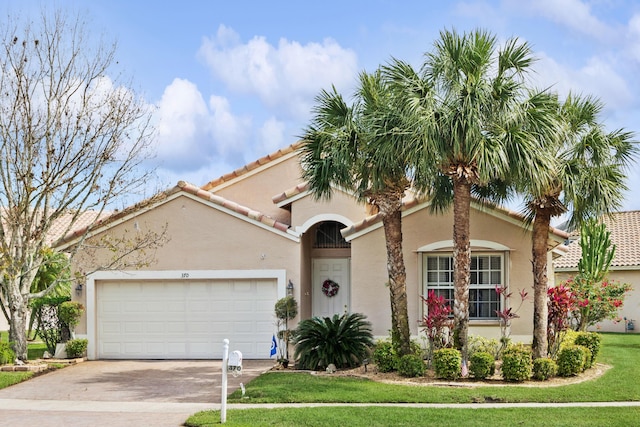 mediterranean / spanish-style home featuring stucco siding, a front yard, a garage, driveway, and a tiled roof