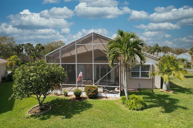 rear view of house featuring stucco siding, a patio area, glass enclosure, and a yard