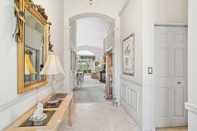 corridor with arched walkways, light tile patterned floors, vaulted ceiling, and light carpet