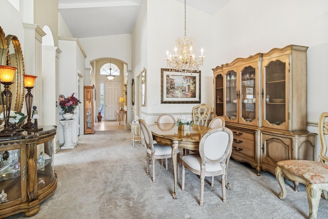 dining area with arched walkways, high vaulted ceiling, light carpet, and an inviting chandelier