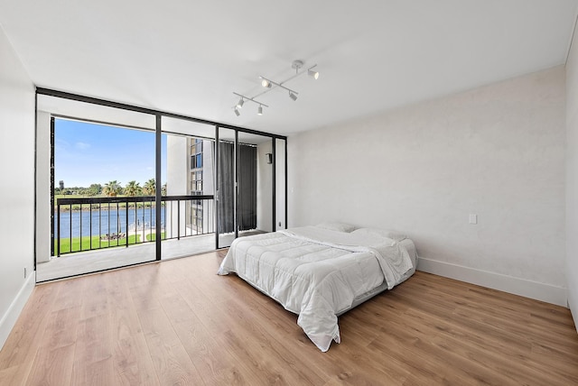 bedroom featuring access to outside, baseboards, a wall of windows, and wood finished floors