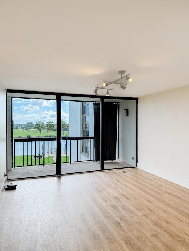 empty room with a water view, baseboards, wood finished floors, and expansive windows