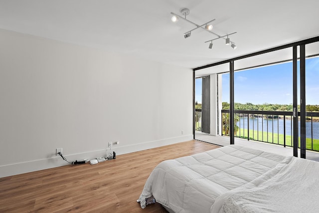 bedroom with wood finished floors, access to exterior, baseboards, a water view, and expansive windows
