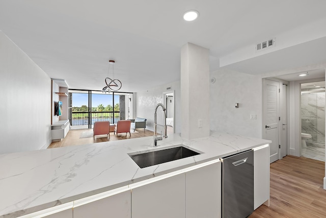 kitchen featuring visible vents, a sink, light wood-style flooring, and light stone counters