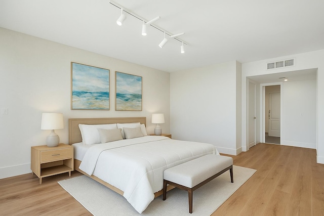 bedroom featuring visible vents, rail lighting, baseboards, and light wood-type flooring