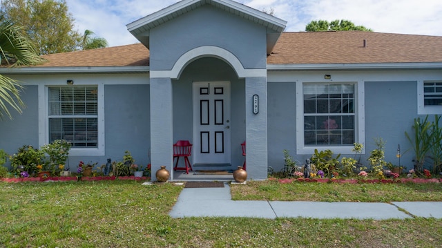 property entrance featuring a lawn, a shingled roof, and stucco siding