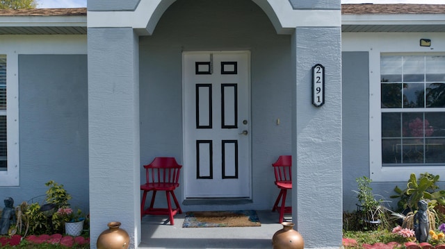 view of exterior entry featuring stucco siding and roof with shingles